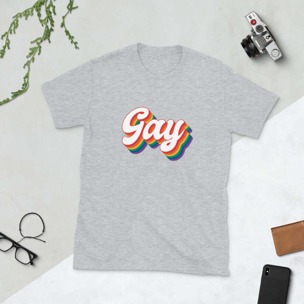 Light grey t-shirt with the word Gay printed on the front. The word gay is outlined in rainbow.