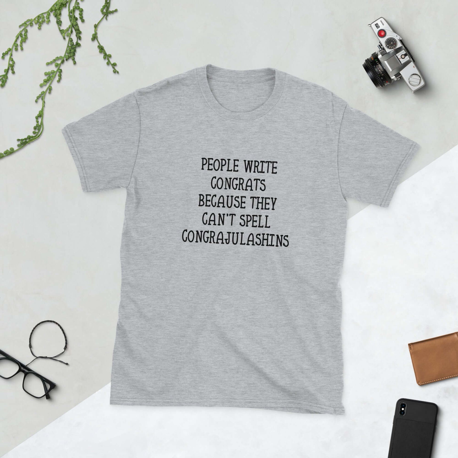 Light grey t-shirt with the words People write congrats because they can't spell congratulations printed on the front. The word congratulations is intentionally misspelled.