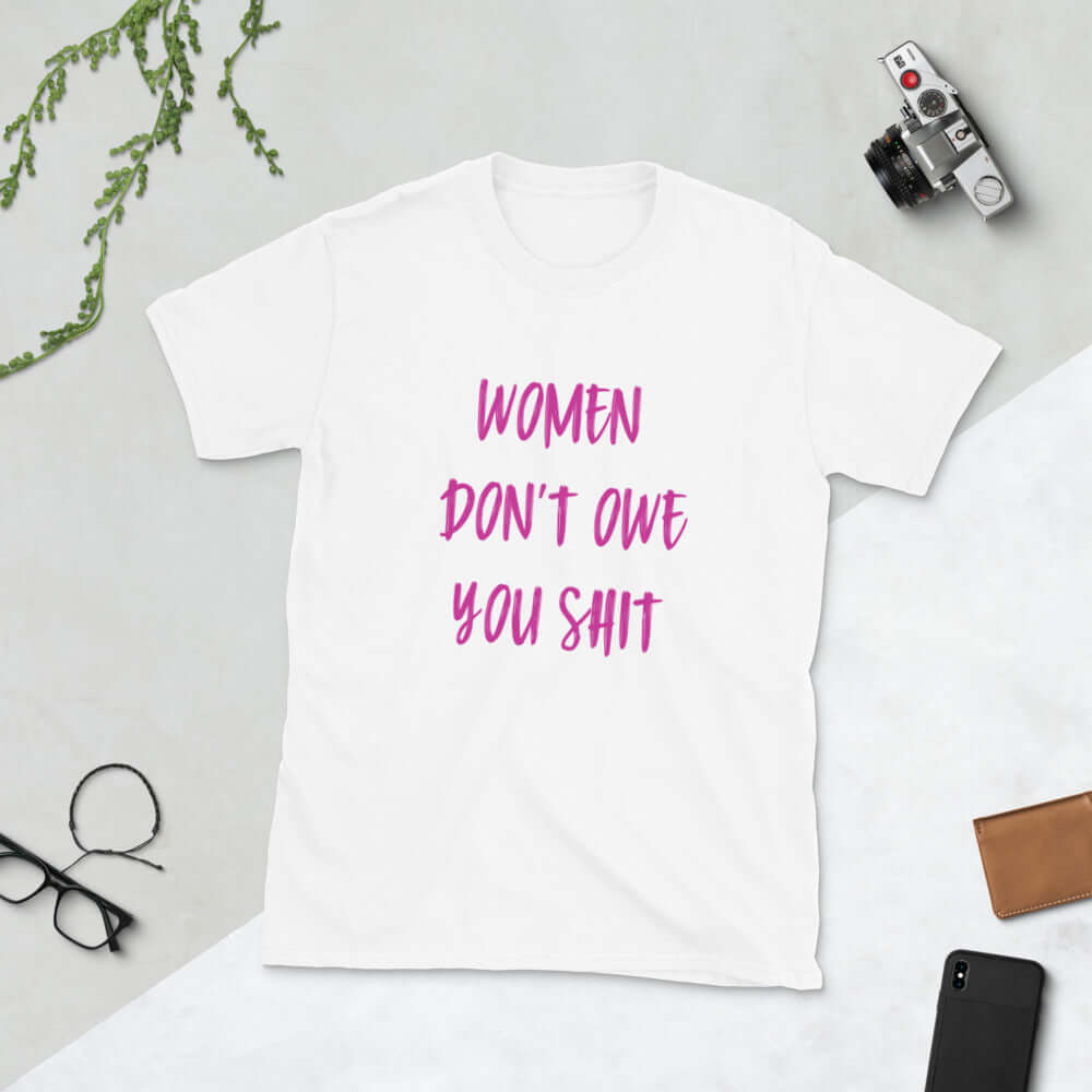 White t-shirt with the words Women don't owe you shit printed on the front in pink.