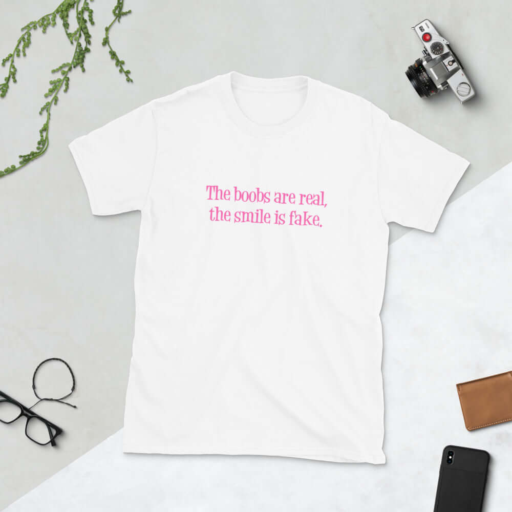White t-shirt with the phrase The boobs are real, the smile is fake printed in pink on the front.