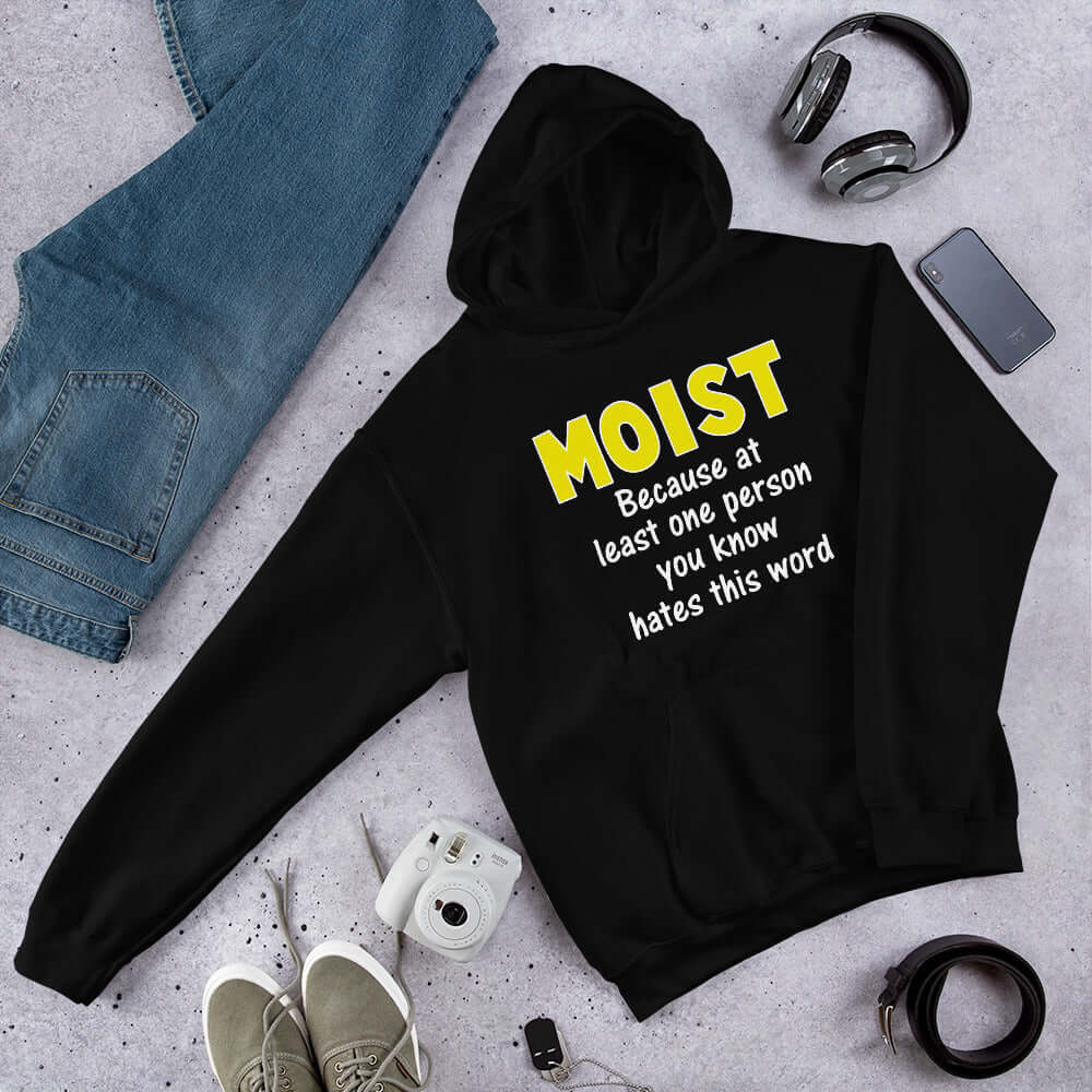 Black hoodie sweatshirt with the word Moist printed in large yellow bold font. In smaller font under the word moist is the phrase Because at least one person you know hates this word. 