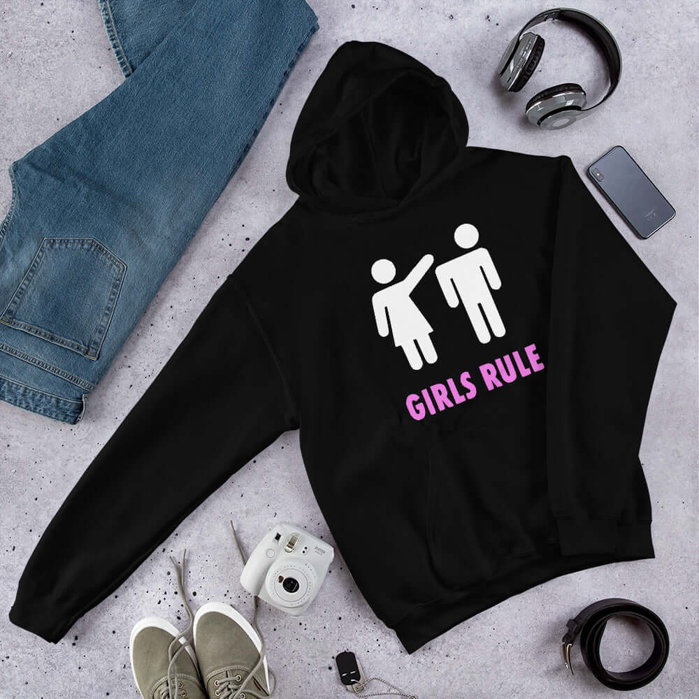 Black hoodie sweatshirt. The sweatshirt has an image of a stick figure man and woman. The woman is punching the mans head off and the words Girls rule is printed beneath in hot pink. The graphics are printed on the front of the hoodie.