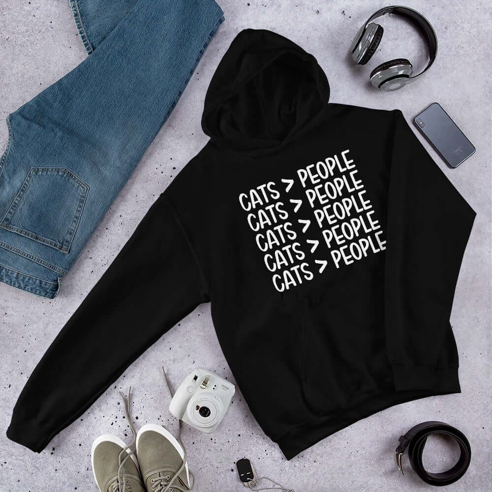 Black hooded sweatshirt with the words Cats > people printed on the front.