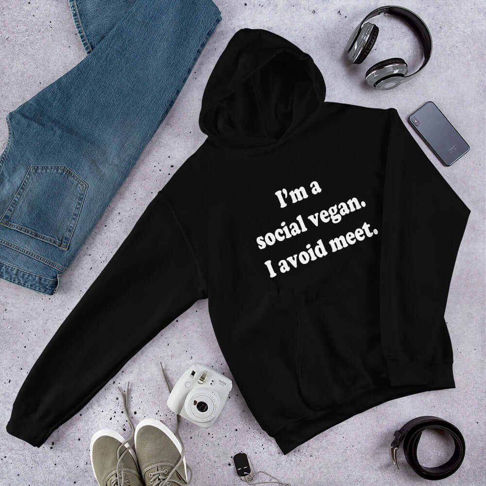 Black hoodie sweatshirt with the pun phrase I'm a social vegan, I avoid meet printed on the front.