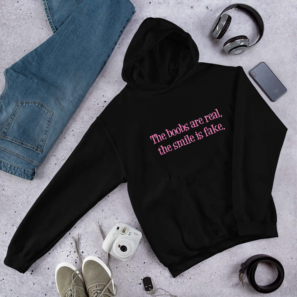 Black hoodie sweatshirt with the phrase The boobs are real, the smile is fake printed in pink on the front.