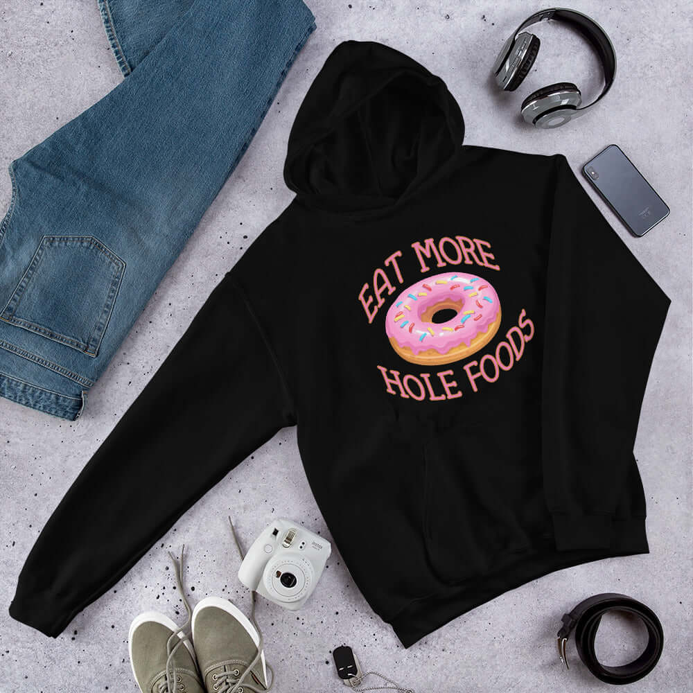 Black hoodie sweatshirt with an image of a donut with pink icing and sprinkles and the words Eat more hole foods printed on the front.