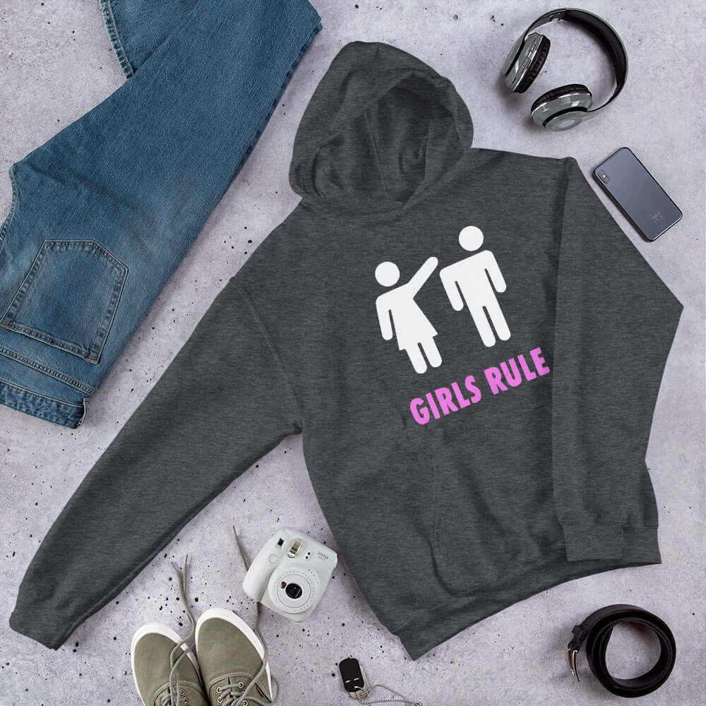Dark grey hoodie sweatshirt. The sweatshirt has an image of a stick figure man and woman. The woman is punching the mans head off and the words Girls rule is printed beneath in hot pink. The graphics are printed on the front of the hoodie.