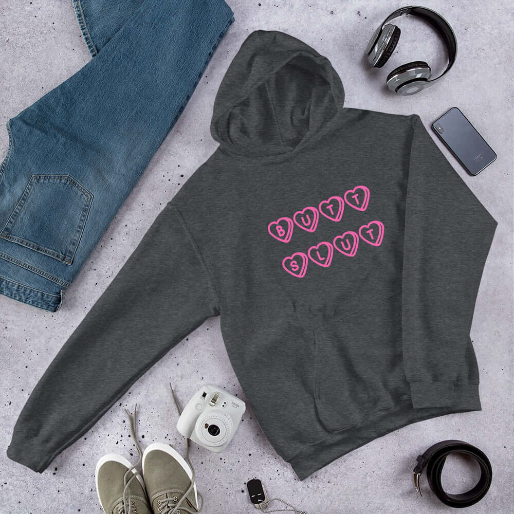Dark grey hoodie sweatshirt with the words Butt Slut printed in pink on the front. Pink hearts are around each letter in the text.