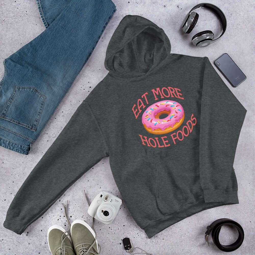 Dark heather grey hoodie sweatshirt with an image of a donut with pink icing and sprinkles and the words Eat more hole foods printed on the front.