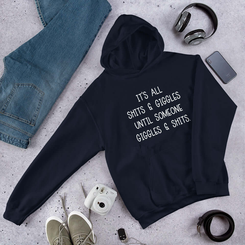 Navy blue hoodie sweatshirt with the words It's all shits & giggles until someone giggles & shits printed on the front.