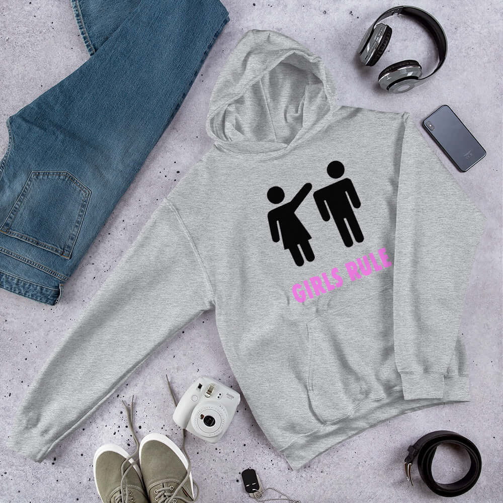 Light grey hoodie sweatshirt. The sweatshirt has an image of a stick figure man and woman. The woman is punching the mans head off and the words Girls rule is printed beneath in hot pink. The graphics are printed on the front of the hoodie.