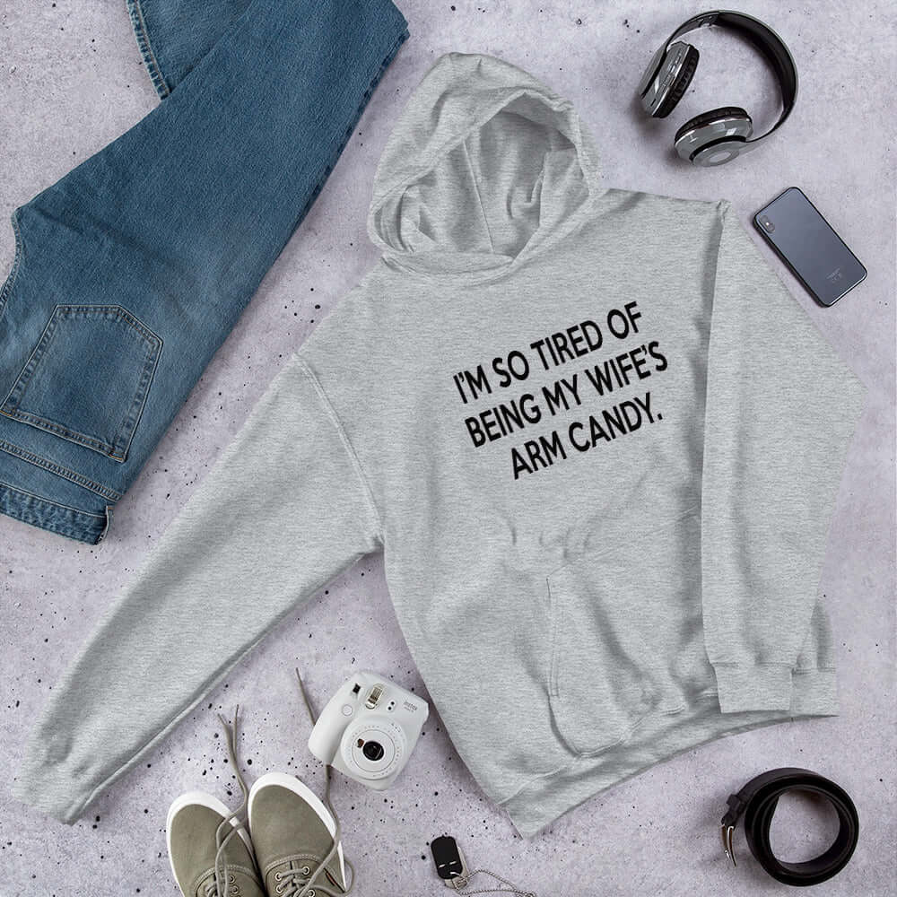 Light grey hoodie sweatshirt with the funny phrase I'm so tired of being my wife's arm candy printed on the front.