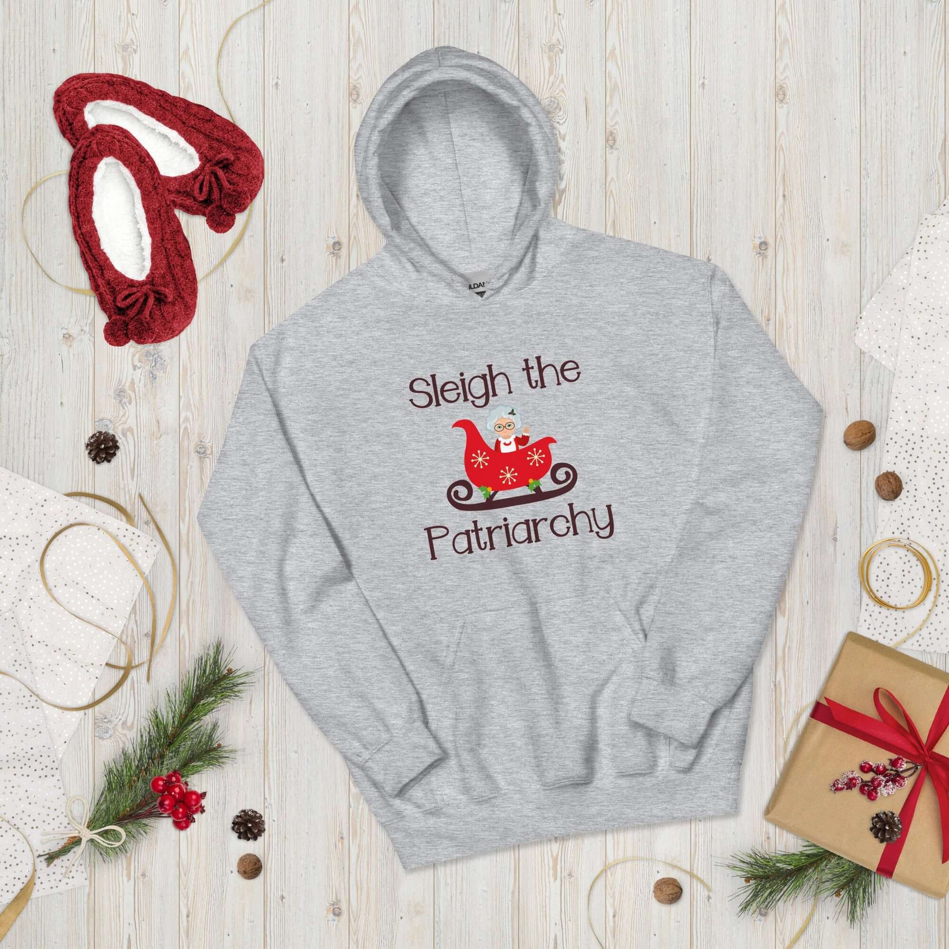 Light grey hooded sweatshirt with graphic of Mrs. Claus sitting in a sleigh and the words Sleigh the patriarchy printed on the front.