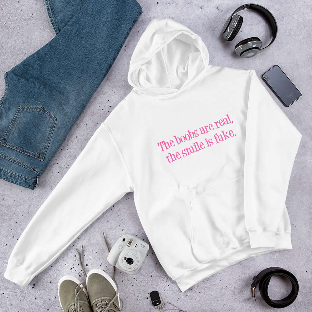 White hoodie sweatshirt with the phrase The boobs are real, the smile is fake printed in pink on the front.
