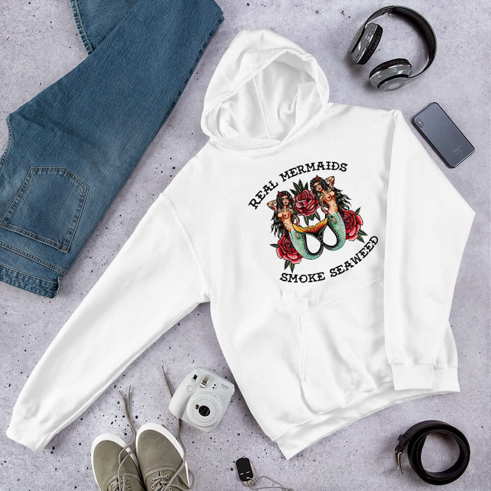 White hooded sweatshirt with image of 2 mermaids and the words Real mermaids smoke seaweed printed on the front.