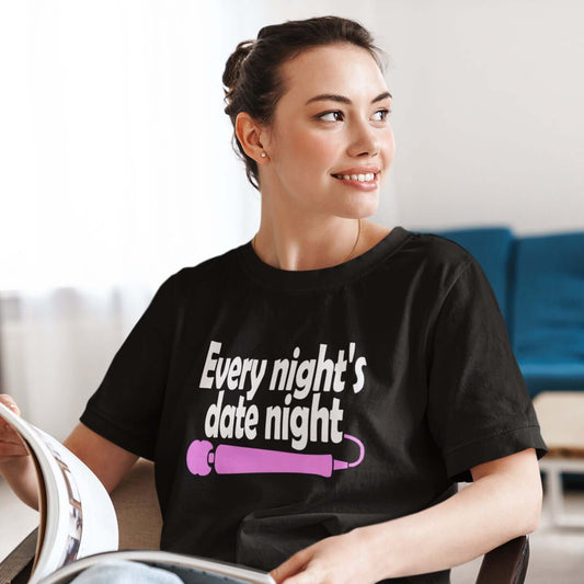 Woman sitting in a chair wearing a black t-shirt with the phrase Every night is date night with a hot pink wand vibrator printed beneath. The graphics are printed on the front of the shirt.