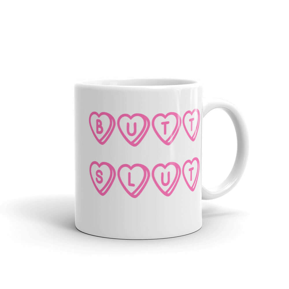 White ceramic mug with the words Butt Slut printed in pink on both sides. Pink hearts are around each letter in the text.