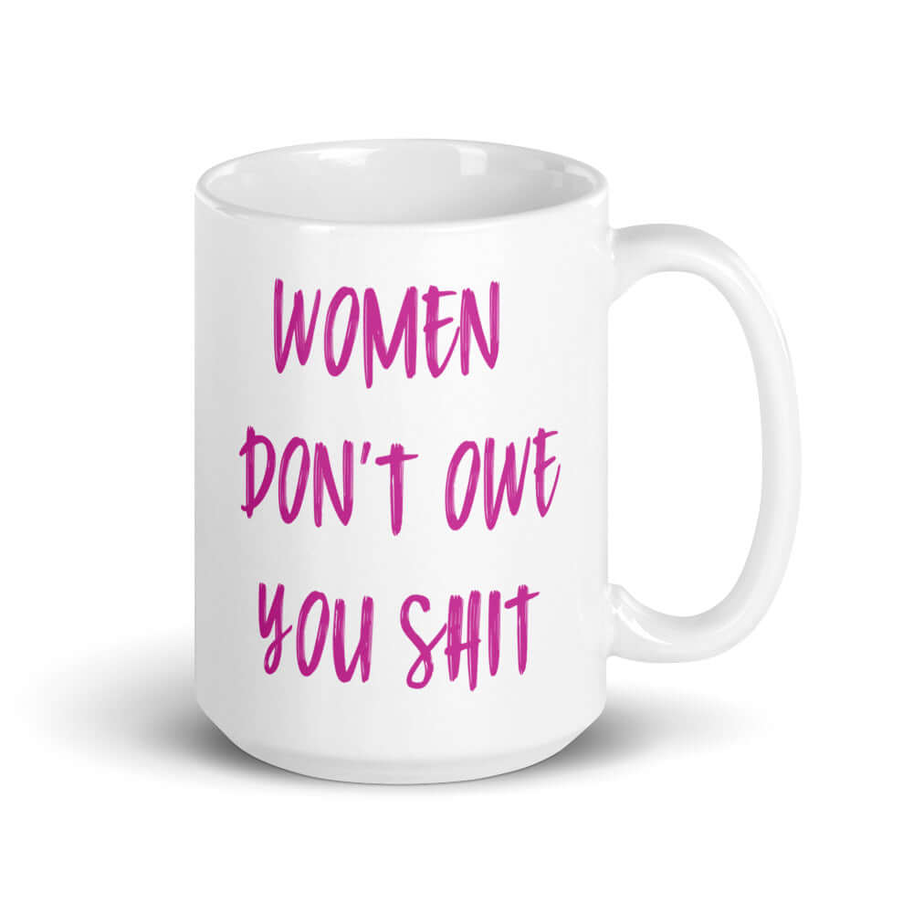 White ceramic coffee mug with the words Women don't owe you shit printed on both sides in pink.