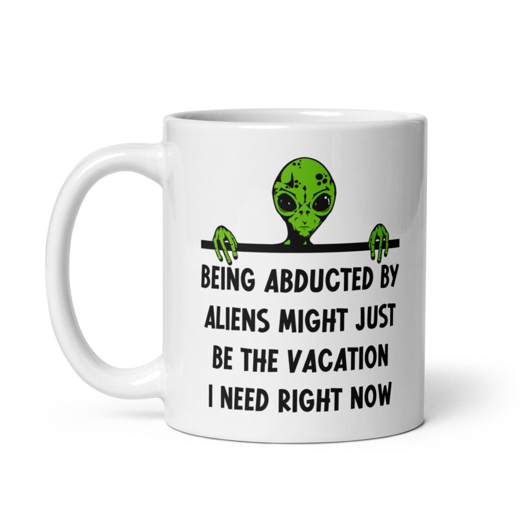 White ceramic mug with image of an alien and the words 'Being abducted by aliens might just be the vacation I need right now' printed on both sides.