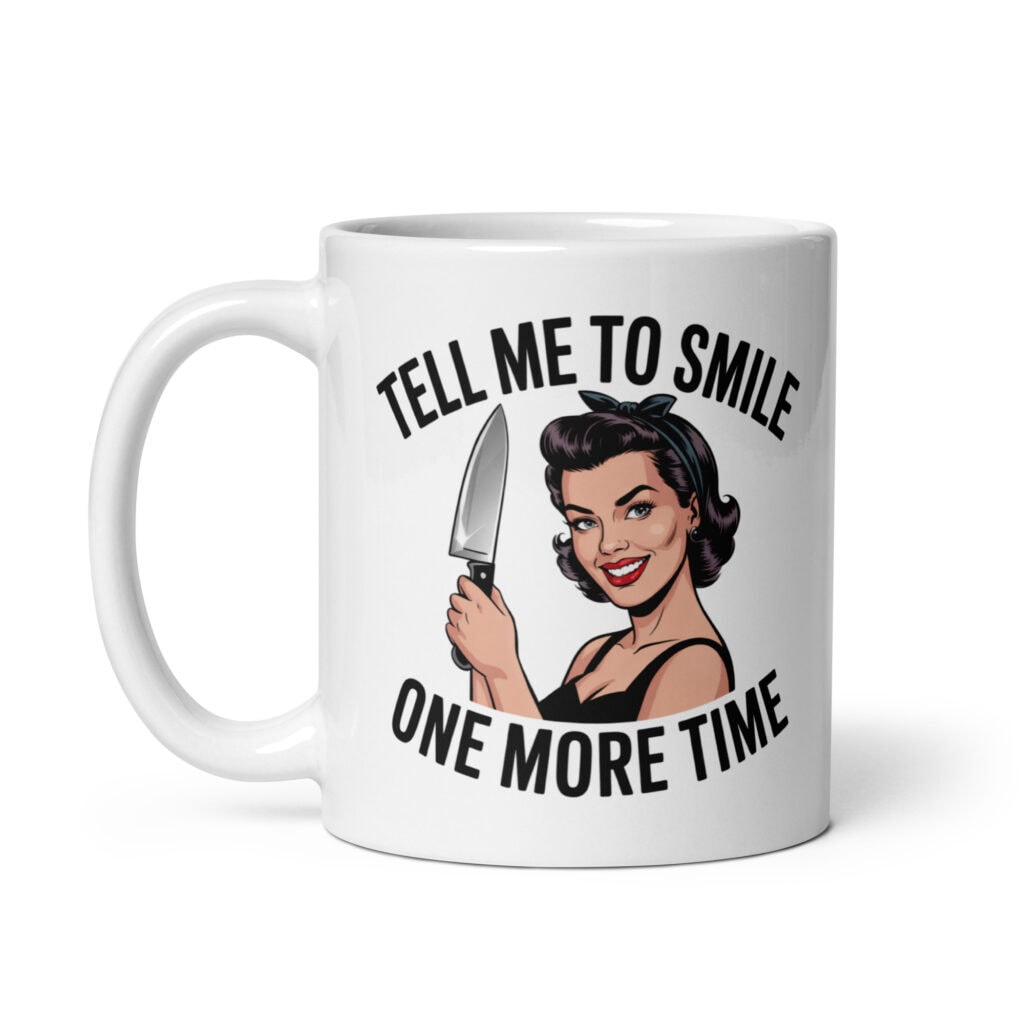 White ceramic mug with graphic of a woman holding a knife and the phrase 'Tell me to smile one more time' printed on both sides.