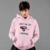 Alternative looking woman with short hair wearing a light pink hoodie sweatshirt. The hoodie has an image of a strap-on dildo and the words 'Just the tip. I promise.' printed on the front.