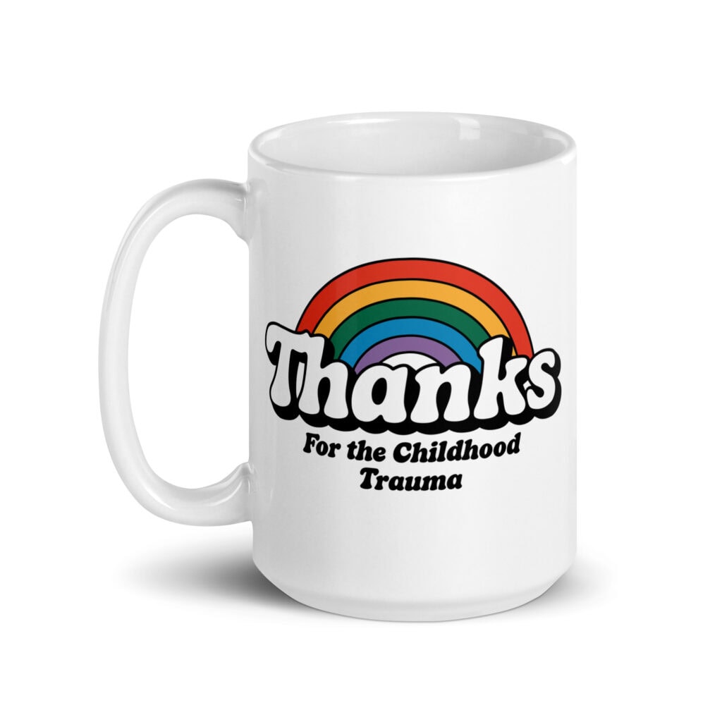 White ceramic mug with a rainbow and the text "Thanks for the childhood trauma' printed on both sides.