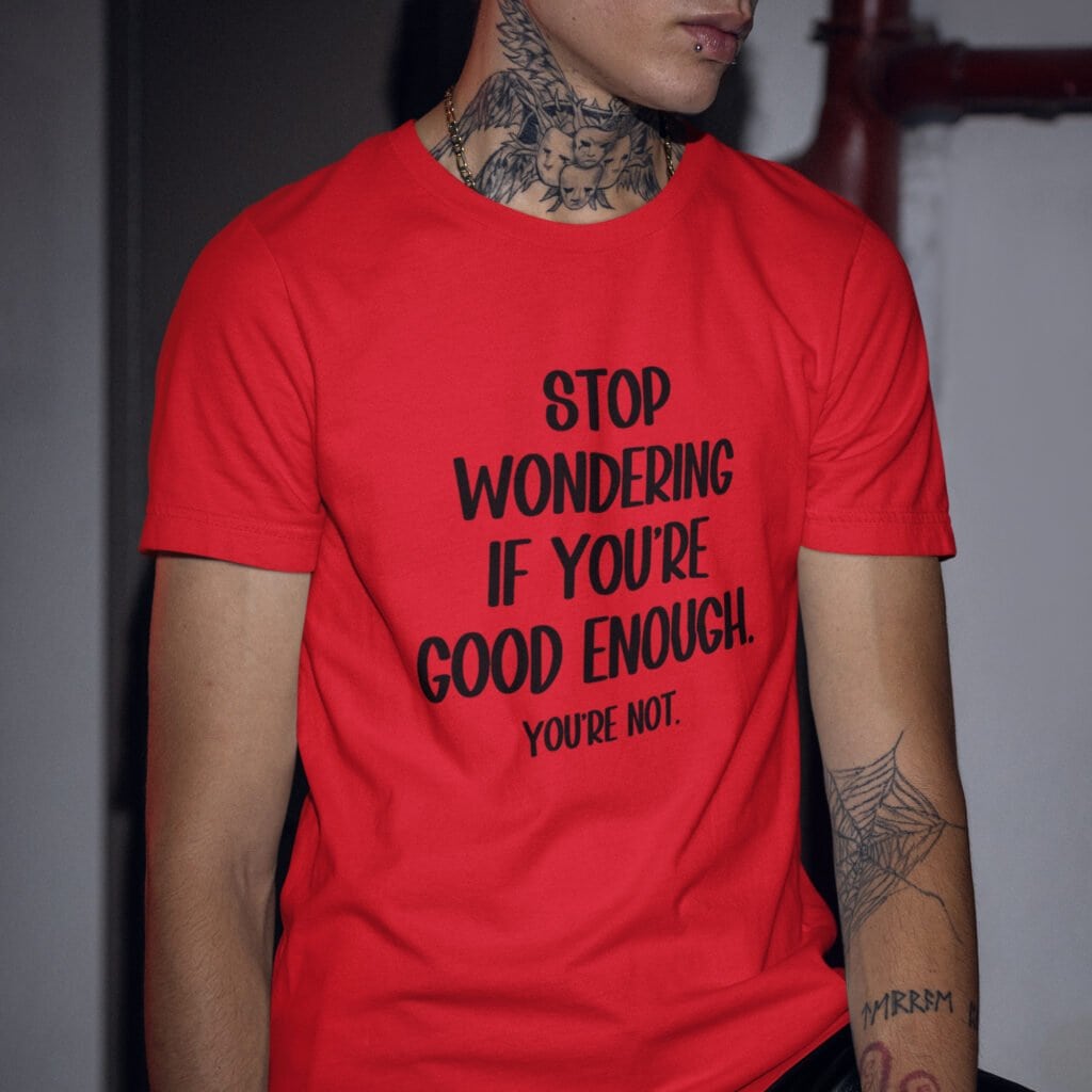 Man wearing a red t-shirt with the phrase 'Stop wondering if you're good enough. You're not.' printed on the front. The words 'You're not' are smaller then the rest.