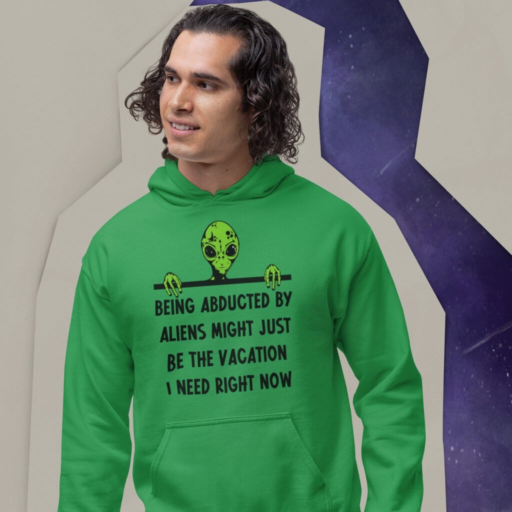 Man wearing a green hoodie sweatshirt with image of an alien and the words 'Being abducted by aliens might just be the vacation I need right now' printed on the front.