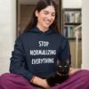 Woman wearing a navy blue hoodie sweatshirt with the text 'Stop normalizing everything' printed on the front.