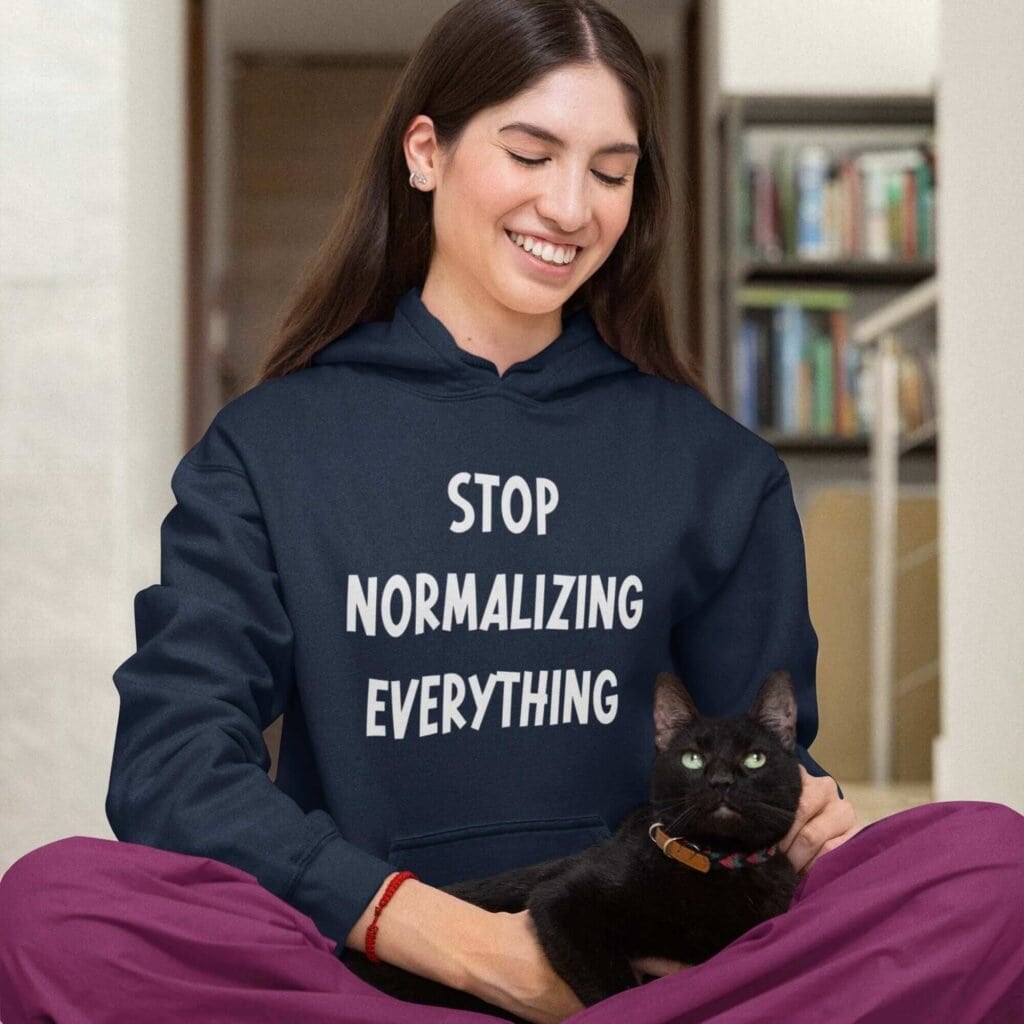Woman wearing a navy blue hoodie sweatshirt with the text 'Stop normalizing everything' printed on the front.