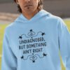 Man wearing a light blue hoodie sweatshirt with the phrase 'Undiagnosed, but something ain't right 'printed on the front. The text is black and has a star graphic embellishment around the words.