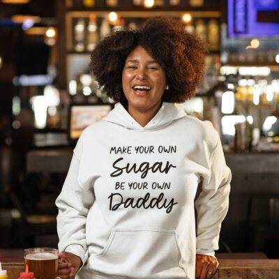 Woman wearing a white hoodie sweatshirt with the text 'Make your own sugar Be your own Daddy' printed on the front.