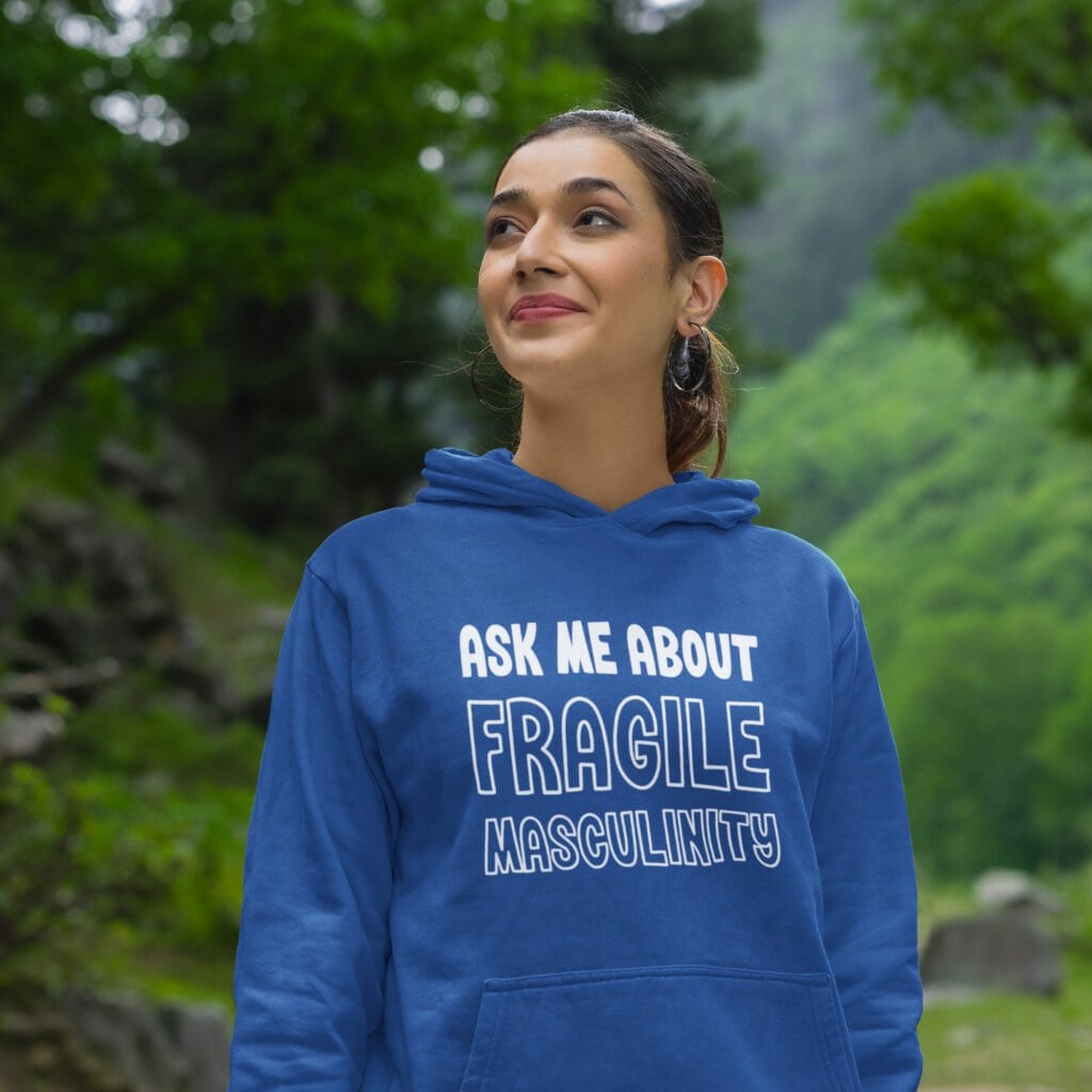 Smiling woman wearing a royal blue hoodie sweatshirt with the text 'Ask me about fragile masculinity' printed on the front.