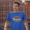 Man wearing a royal blue t-shirt with an image of a rainbow and the words 'Thanks for the childhood trauma' printed on the front. The word Thanks is large and the rest of the words are smaller under.