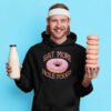 Man holding a stack of donuts and a bottle of milk. He is wearing a black hoodie sweatshirt with an image of a donut with pink icing and sprinkles and the text 'Eat more hole foods' printed on the front.