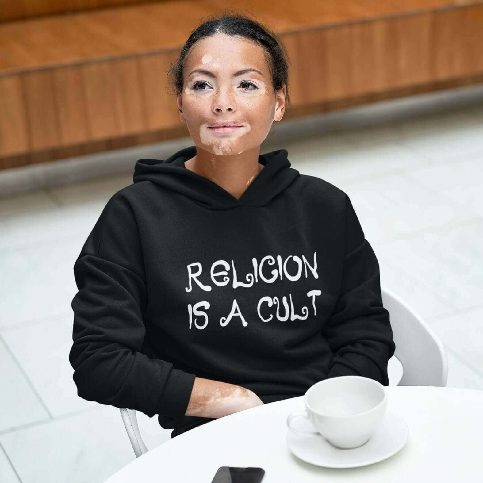 Woman wearing a black hoodie sweatshirt with the text 'Religion is a cult' printed on the front.