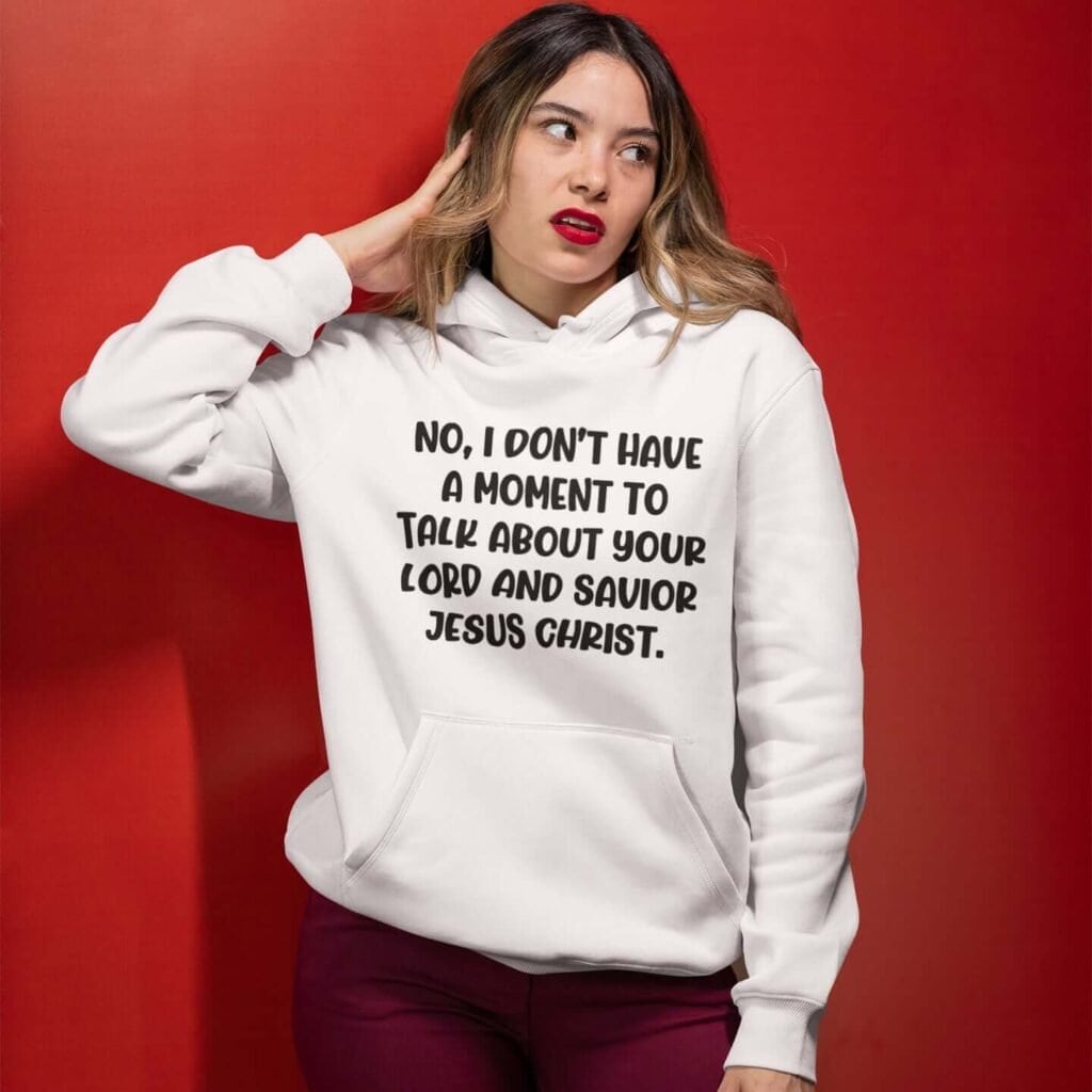 Annoyed looking woman wearing a white hoodie sweatshirt with the phrase 'No, I don't have a moment to talk about your lord and savior Jesus Christ.' printed on the front.