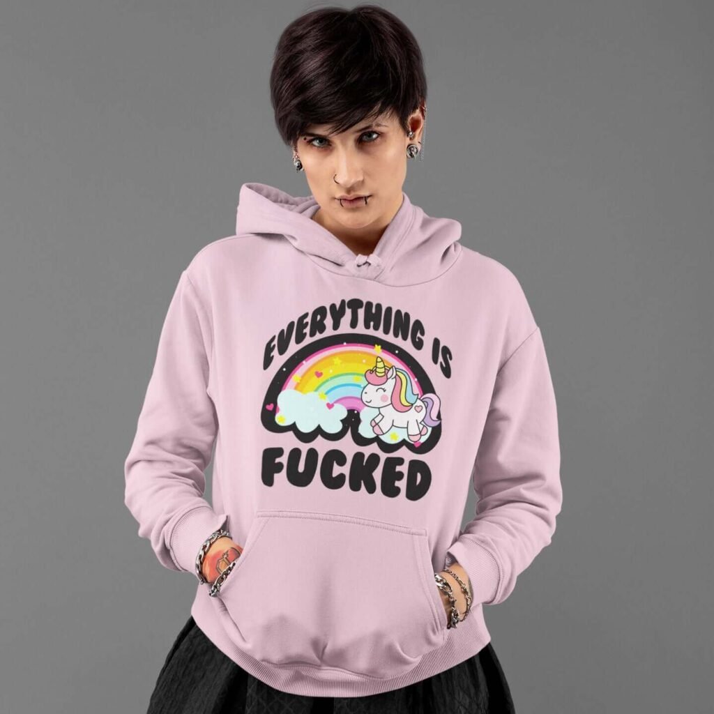 Edgy woman wearing a pink hoodie sweatshirt. The hoodie has a graphic of a kawaii style unicorn and a pastel rainbow with the text 'Everything is fucked' printed on the front.