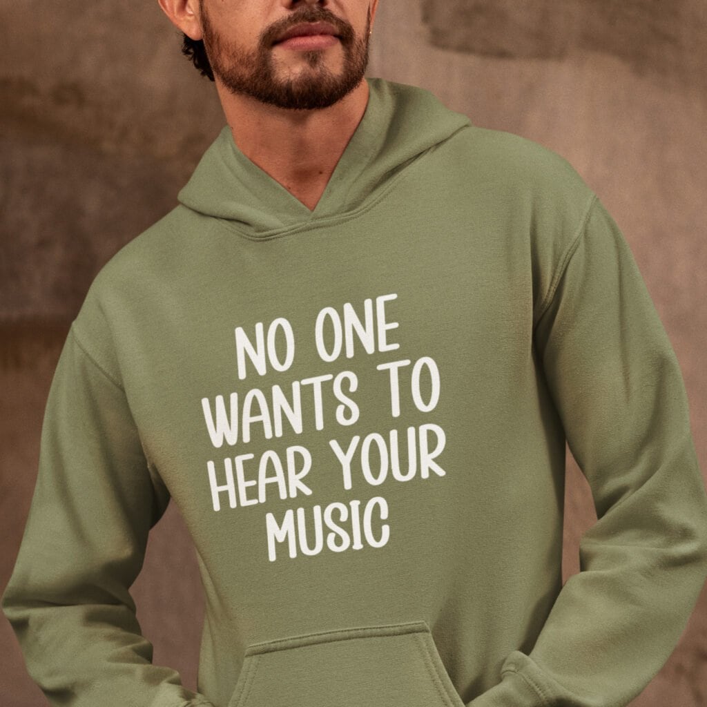 Man wearing a military green hoodie sweatshirt with the text 'No one wants to hear your music' printed on the front.