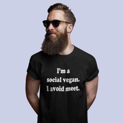 Man wearing sunglasses and a black t-shirt with the pun phrase 'I'm a social vegan. I avoid meet.' printed on the front.