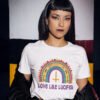 Woman wearing a white t-shirt with an image of a boho style rainbow. There is an upside down cross in the center arch of the rainbow and the text 'Love like Lucifer' printed under. The graphics are printed on the front.