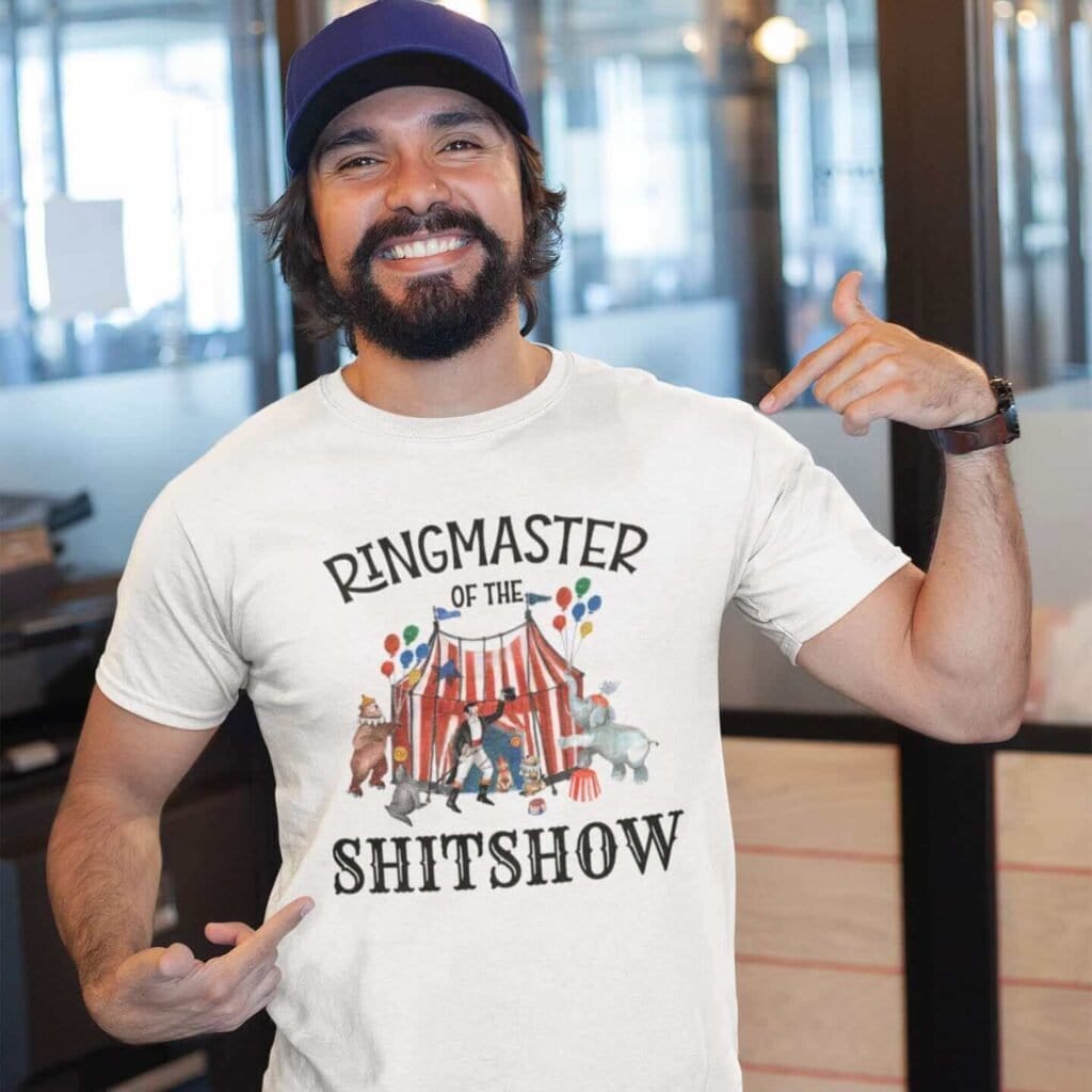 Man wearing a white t-shirt with a circus theme graphic and the text 'Ringmaster of the Shitshow' printed on the front.