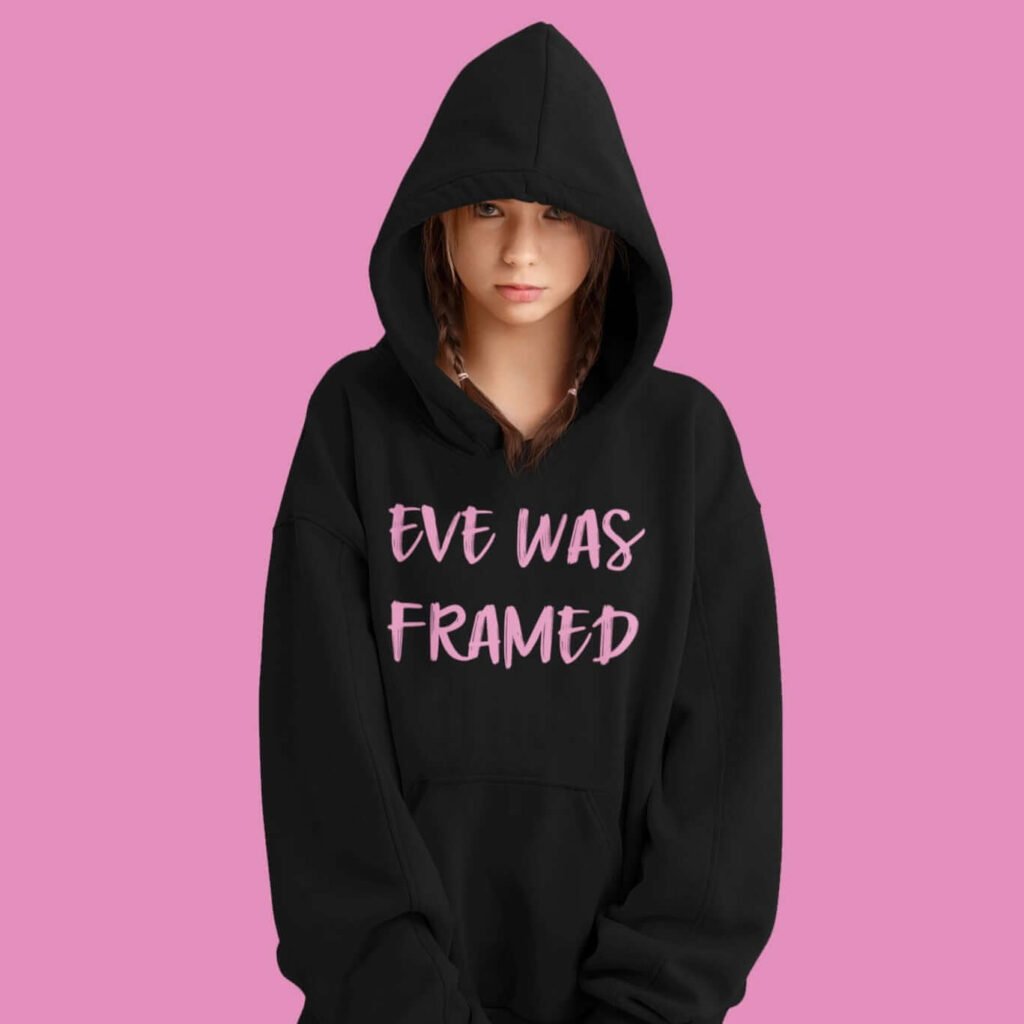 Young woman wearing black hoodie sweatshirt with the text 'Eve was framed' printed on the front in pink.