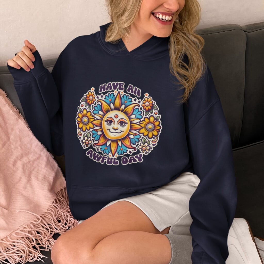 Smiling woman sitting on sofa wearing a navy blue hoodie sweatshirt with a sun graphic and the text 'Have an awful day' printed on the front.