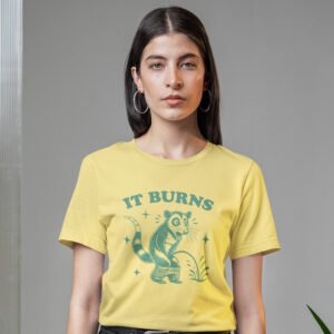 Woman wearing a yellow t-shirt with an image of an opossum peeing. The words 'It burns' are printed above.