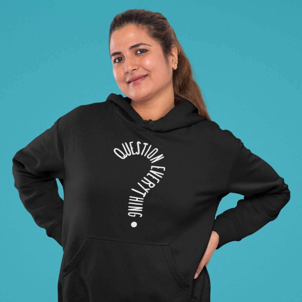 Woman wearing a black hoodie sweatshirt with the text 'Question everything' printed on the front. The words are in the shape of a question mark.