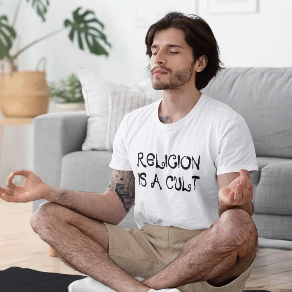 Man meditating while wearing a white t-shirt with the text 'Religion is a cult' printed on the front.
