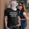 Tattooed bearded man wearing a black t-shirt with the funny phrase 'I'm so tired of being my wife's arm candy' printed on the front.