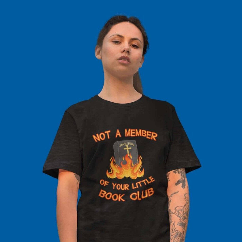 Woman wearing a black t-shirt with image of a burning bible and the text 'Not a member of your little book club' printed on the front.