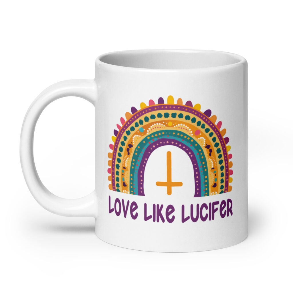 White ceramic mug with an image of a boho style rainbow. There is an upside down cross in the center arch of the rainbow and the text 'Love like Lucifer' printed under. The graphics are printed on both sides of the mug.